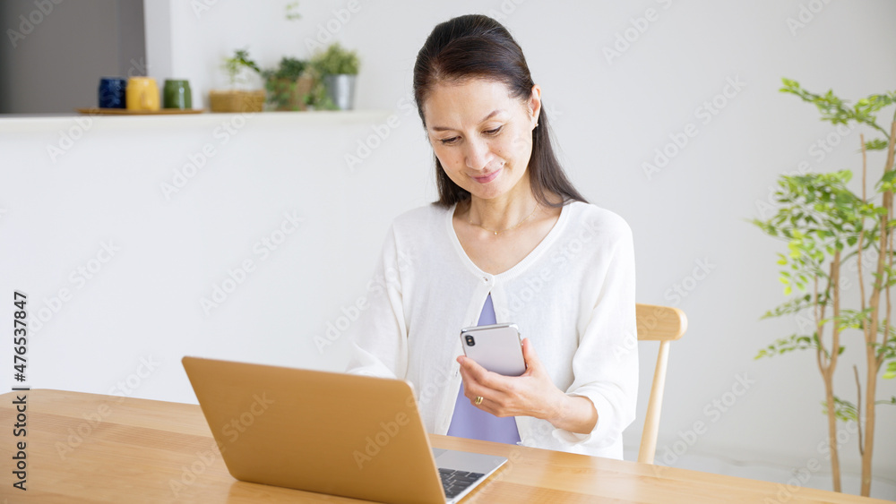 スマホを見ながらパソコンに入力するシニア女性