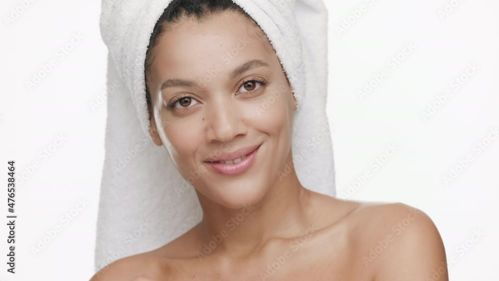Gorgeous African American young slim woman with a towel on hair and nude shoulders strokes jaw line turning head to the camera and smiles wide on white background | Sagging jowls prevention concept Gorgeous African American young slim woman with a towel on hair and nude shoulders strokes jaw line turning head to the camera and smiles wide on white background | Sagging jowls prevention concept