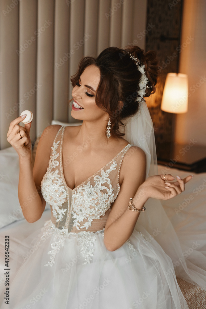 Stunning young woman in a bridal dress enjoying tasty dessert while sitting on the bed Stunning young woman in a bridal dress enjoying tasty dessert while sitting on the bed