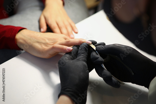 Nail master cutting off cuticle on clients hands with special equipment