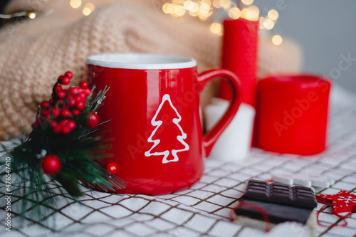 Red mug with coffee in Christmas decorations on a white checkered blanket. New year  garlands  gifts  candles - an atmosphere of warmth  comfort and magic.