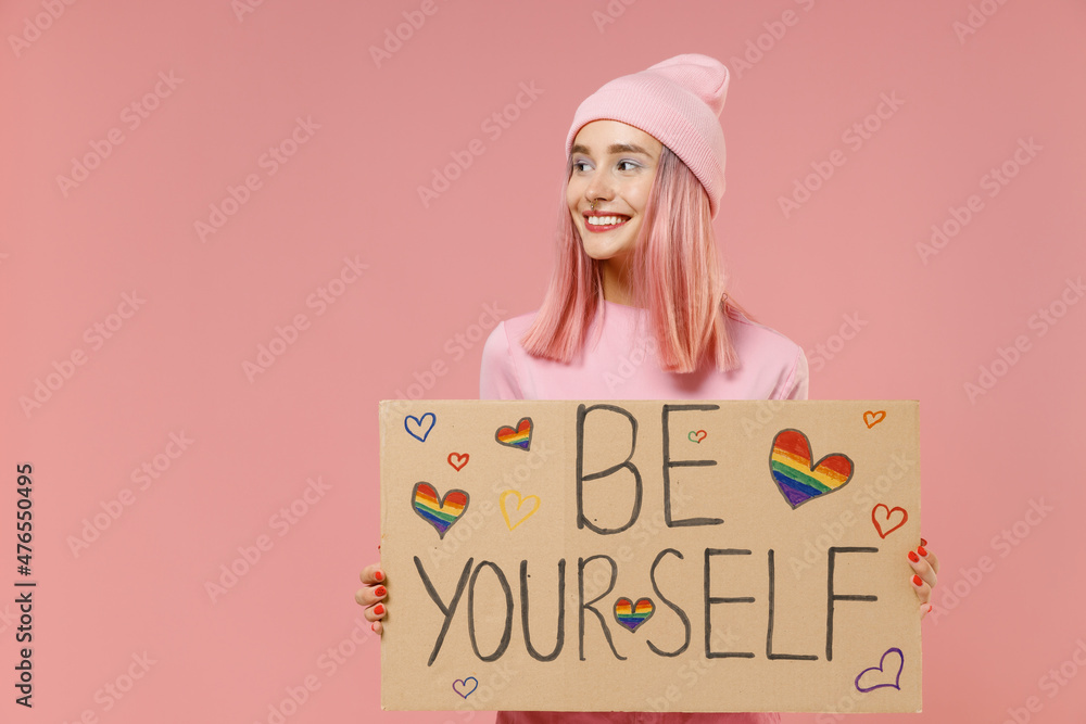 Φωτογραφία Young lesbian woman with bright dyed rose hair in rosy top shirt hat hold card sign with be yourself title text isolated on plain light pastel pink background studio