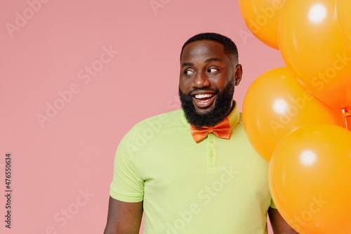 Young smiling black gay man 20s in green t-shirt hold bunch of air inflated helium balloons celebrating birthday party look aside on copy space area isolated on plain pastel pink background studio © ViDi Studio