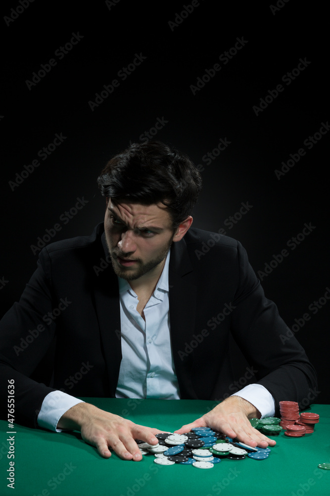 Concentrated Handsome Caucasian Brunet Young Pocker Player At Pocker Table With Chips And Cards While Drinking Alcohol. Concentrated Handsome Caucasian Brunet Young Pocker Player At Pocker Table With Chips And Cards While Drinking Alcohol.