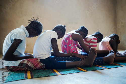 Side view of a group of frightened black African village girls sitting on the floor waiting for their turn during a collective circumcision ritual photo