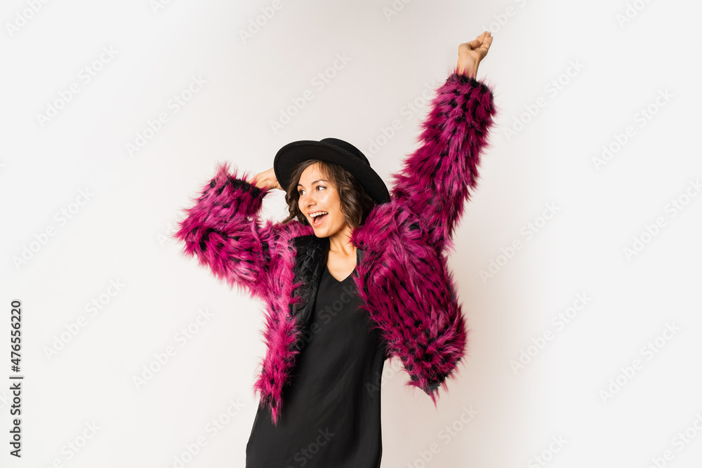Fashionable happy model in winter pink fur coat dancing and having fun on white background. New year party mood. Black hat. Fashionable happy model in winter pink fur coat dancing and having fun on white background. New year party mood. Black hat.