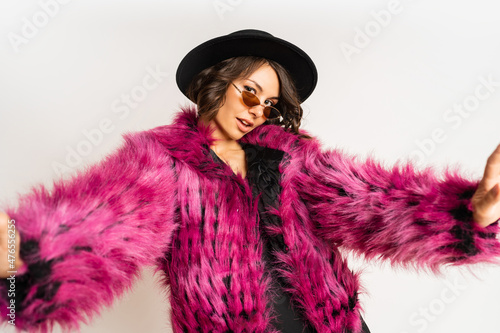 Fashionable happy model in winter pink  fur coat posing on white background.  New year party mood. Black hat.