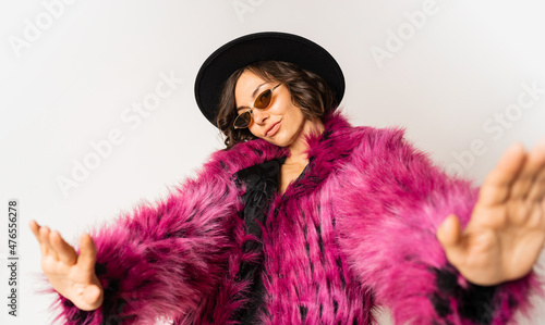 Fashionable happy model in winter pink  fur coat posing on white background.  New year party mood. Black hat.