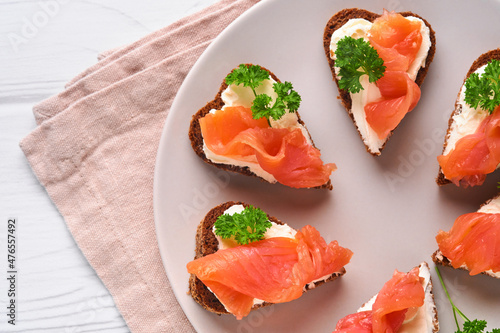 Mini sandwiches with salmon, curd cheese, parsley and rye bread in form of hearts. Valentine's day homemade creative food. Love breakfast design. Selective focus and copy space