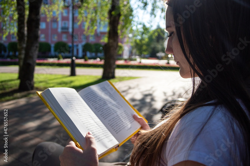 An adult girl sits on a bench and reads a book. Close-up. Selective focus.