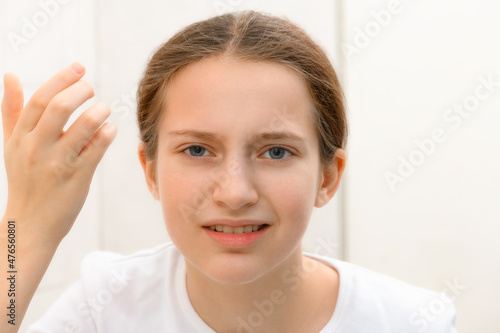 face of teenage girl, she looks at herself in the mirror and touches her face with her hand, she is upset and has frustrated emotions