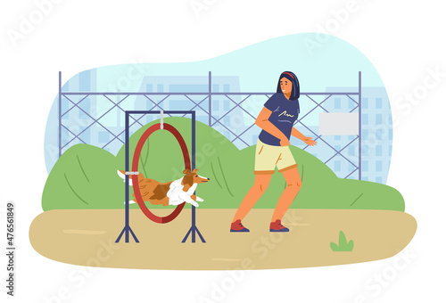 Woman training her sheltie dog on agility field. Dog jumping trough agility ring owner running alongside.