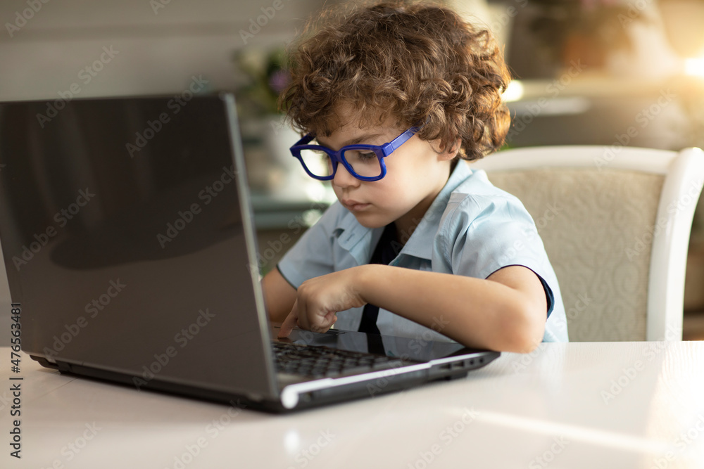 Curly boy in glasses is engaged in a laptop book, carefully looks at the monitor Curly boy in glasses is engaged in a laptop book, carefully looks at the monitor