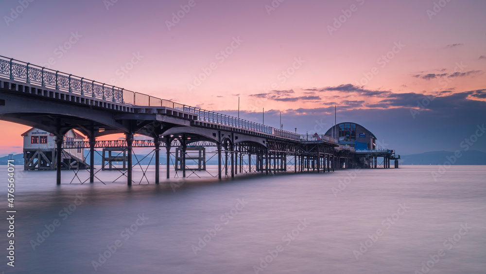 The long pier in the Mumbles, Swansea, south Wales. The wooden and steel structure sits in a calm sea, with a red sky behind it, at sunrise