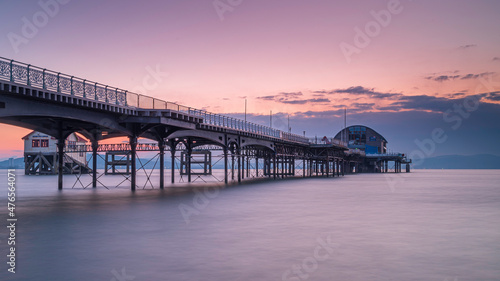 The long pier in the Mumbles, Swansea, south Wales. The wooden and steel structure sits in a calm sea, with a red sky behind it, at sunrise photo