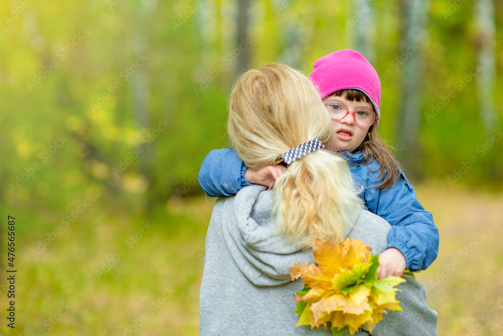 Mother holds in her arms daughter with Downs syndrom at autumn park. Empty space for text Mother holds in her arms daughter with Downs syndrom at autumn park. Empty space for text