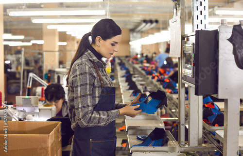Fotografía Side view of shoe factory worker standing in big sewing workshop and checking quality of unfinished details of future sneakers