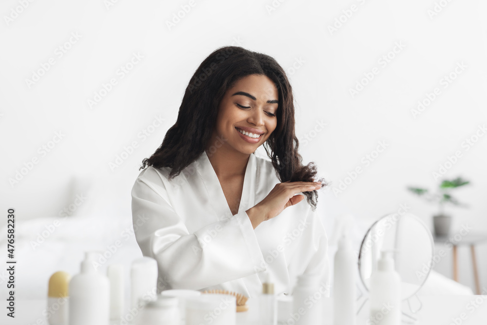 Cosmetics and spa day. Happy african american woman touching her hair and looking in mirror at home Cosmetics and spa day. Happy african american woman touching her hair and looking in mirror at home