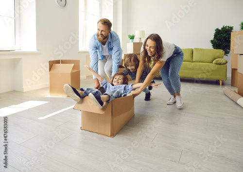 Husband and wife with children who have just moved into their own house are having fun and rejoicing. Parents ride their little sons in cardboard box. Concept of buying your own home and moving.
