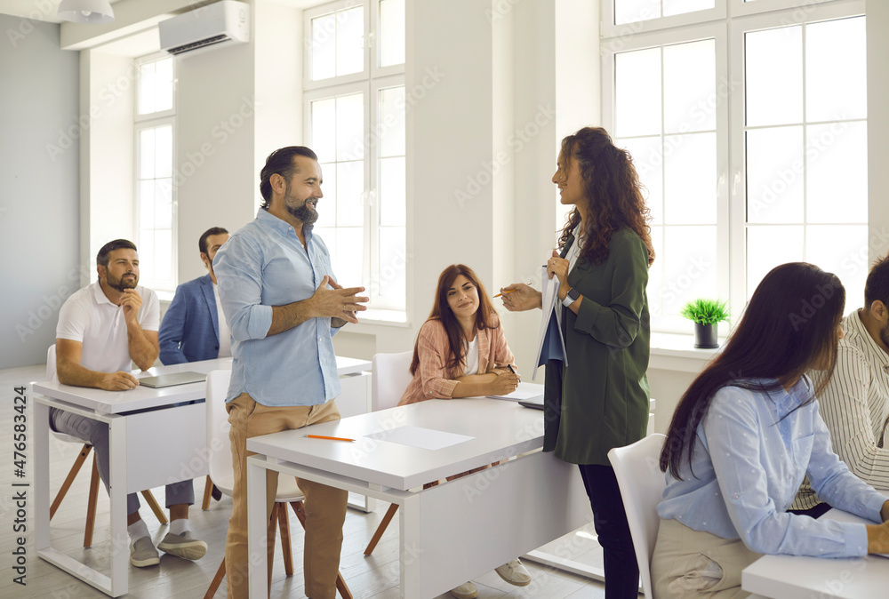 Course trainer, psychologist or business coach training group of people. Adult Caucasian students sitting at tables in classroom, answering teacher's questions, learning new things. Education concept Course trainer, psychologist or business coach training group of people. Adult Caucasian students sitting at tables in classroom, answering teacher's questions, learning new things. Education concept
