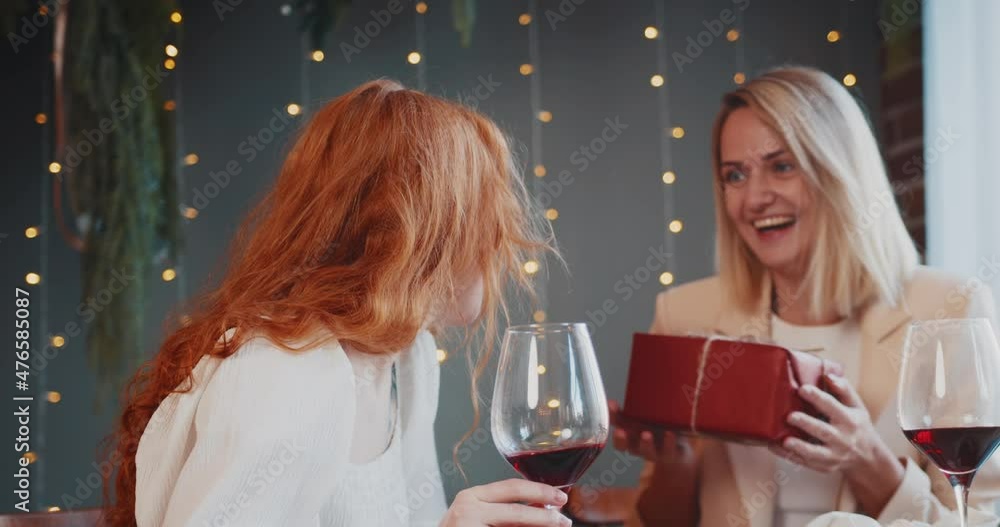 two young women in a restaurant. one gives the other a gift. concept of congratulations on valentine's day. lgbtq+ couple two young women in a restaurant. one gives the other a gift. concept of congratulations on valentine's day. lgbtq+ couple