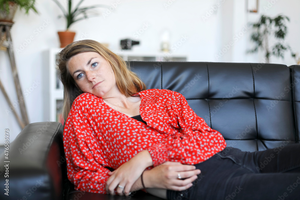 Young blond female relaxing on couch at home while looking away pensive Young blond female relaxing on couch at home while looking away pensive