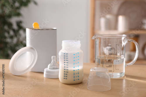 Feeding bottle with infant formula, can and jug of water on wooden table indoors. Baby milk