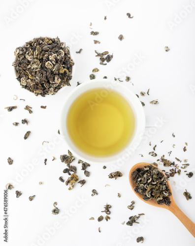 White mug with green tea on a white background. Tea leaves and a wooden spoon.