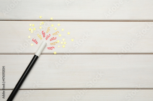 Beautiful black magic wand and confetti on white wooden table, flat lay. Space for text