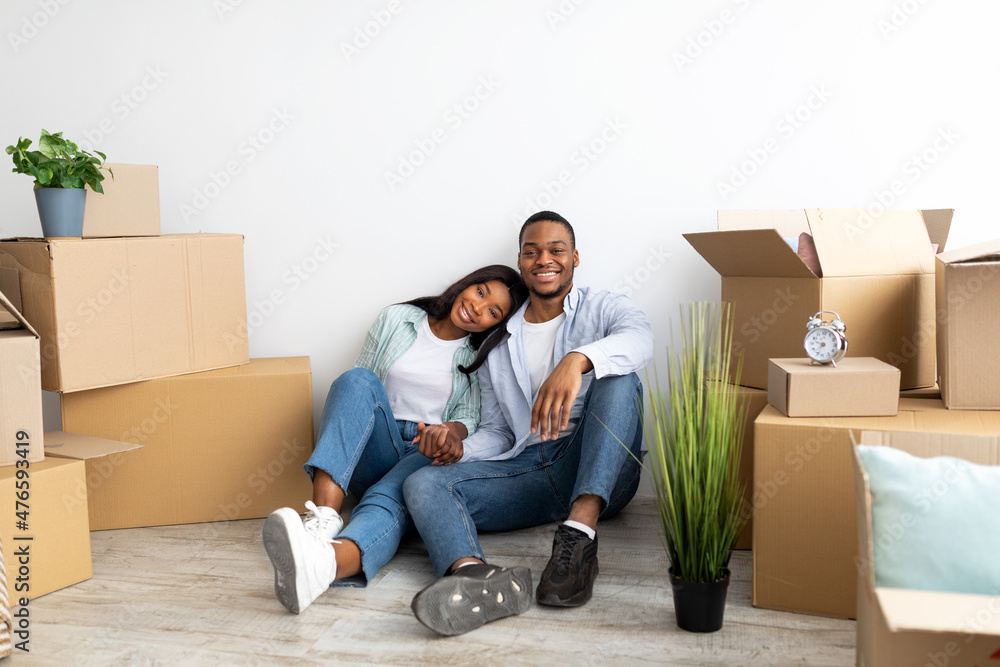 Real estate rent concept. Loving african american spouses relocating to new apartment, sitting among cardboard boxes Real estate rent concept. Loving african american spouses relocating to new apartment, sitting among cardboard boxes