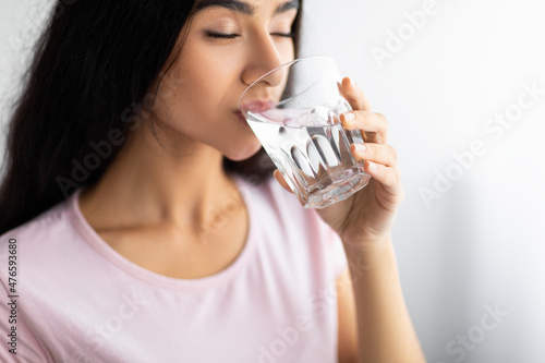 Fotografia Young Indian woman drinking clear mineral water from glass at home, selective focus