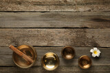 Golden singing bowls, mallet and flower on wooden table, flat lay. Space for text