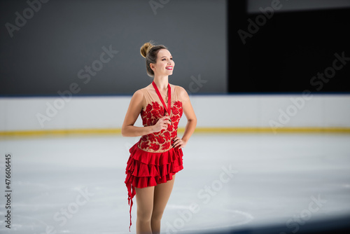 positive figure skater in red dress holding golden medal and posing with hand on hip photo