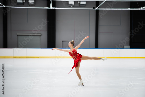 full length of figure skater in red dress performing camel spin in professional ice arena photo