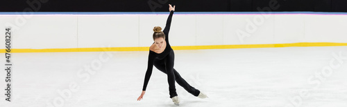 full length of professional figure skater in black bodysuit skating with outstretched hands in ice arena, banner photo