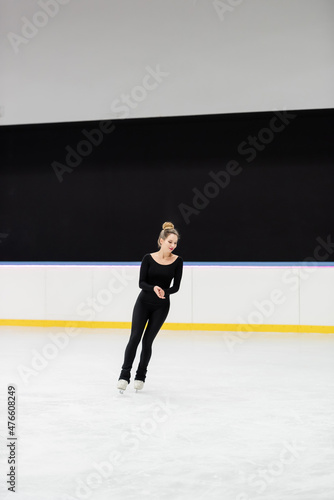 full length of cheerful professional figure skater in black bodysuit skating in ice arena