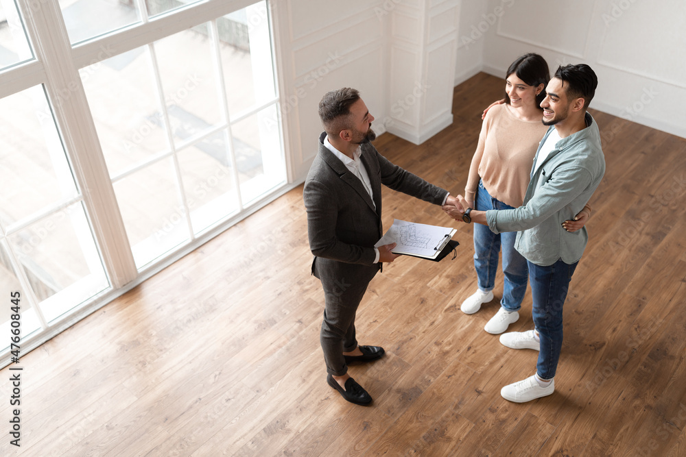 Couple Buying New Apartment, Shaking Hands With Realtor Couple Buying New Apartment, Shaking Hands With Realtor