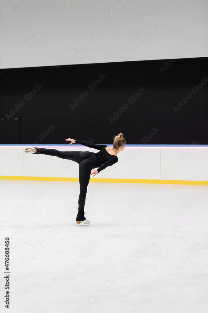 back view of professional figure skater in black bodysuit skating with outstretched hand in ice arena back view of professional figure skater in black bodysuit skating with outstretched hand in ice arena