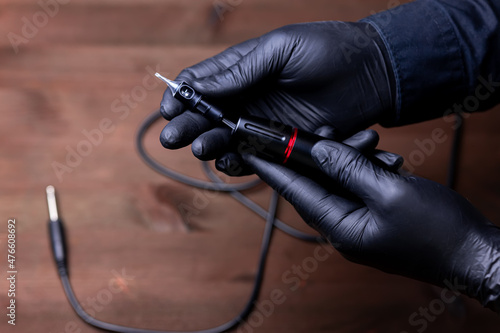 the hands of the permanent makeup master in black medical gloves are placed in a disposable cartridge in a tattoo machine