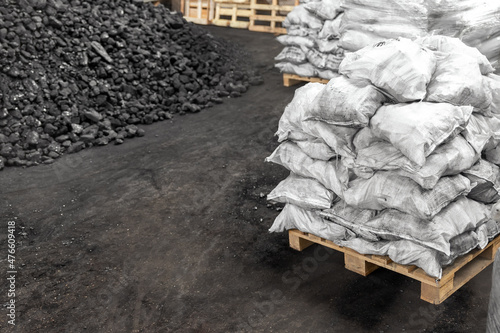 Big heap of dark black lump coal on floor bulk. Charcoal sorage at warehouse stock reserve. activated anthracite packed in plastic bag sack on wooden pallet. Industrial and mining industry background photo