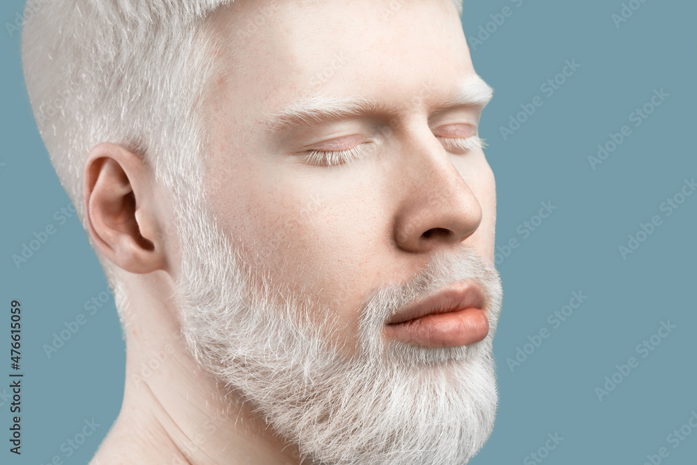 Obraz premium Handsome extraordinary albino guy with pale skin and white hair posing with closed eyes against turquoise background