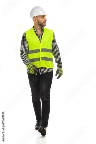 Young man is walking in white hardhat, reflective vest and gloves and looking to the side Fototapeta