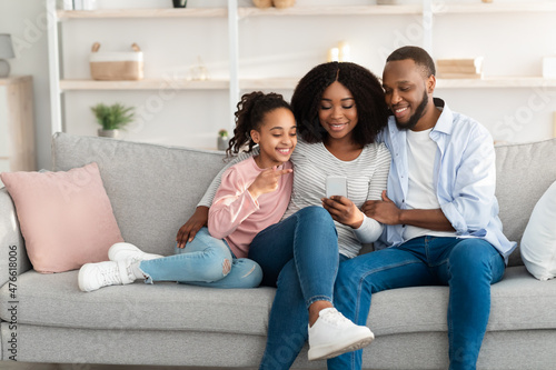 Happy african american family holding and using smartphone at home