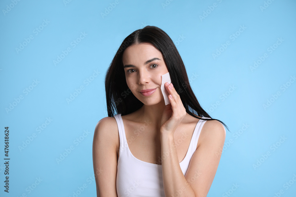 Beautiful woman using mattifying wipe on light blue background Beautiful woman using mattifying wipe on light blue background