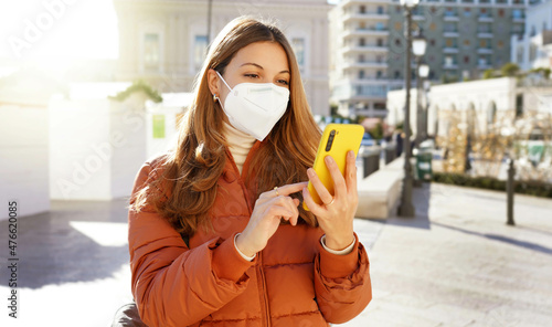 Woman in puffer jacket and medical face mask using her mobile phone outdoors photo