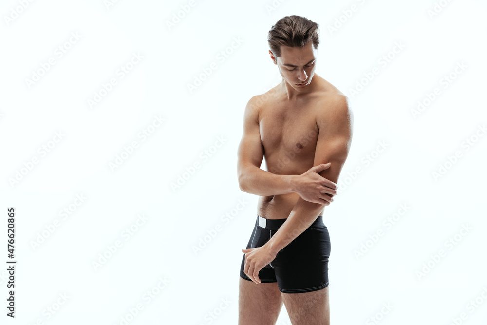 Half-length portrait of young handsome shirtless sportive man wearing black boxer-briefs standing isolated on white background.