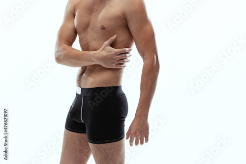 Side view. Cropped portrait of young handsome shirtless sportive man wearing black boxer-briefs standing isolated on white background.