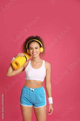 Beautiful African American woman with yoga mat and headphones on pink background