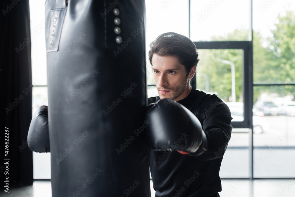 Sportsman in boxing gloves training with punching bag in sports center