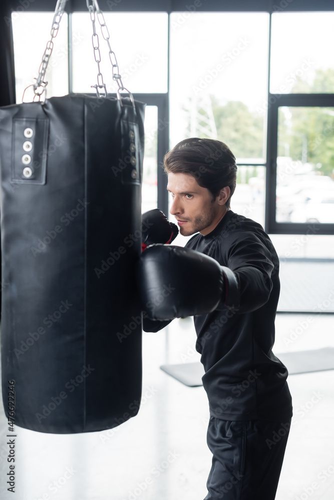 Sportsman in sportswear training with punching bag in gym